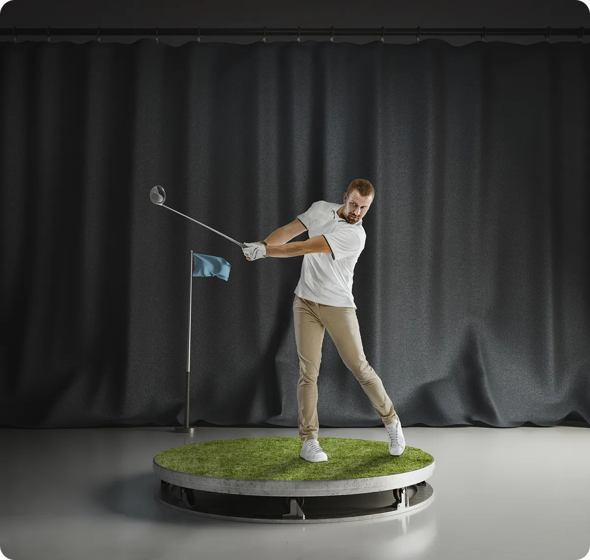 Golfer swinging club indoors on platform.